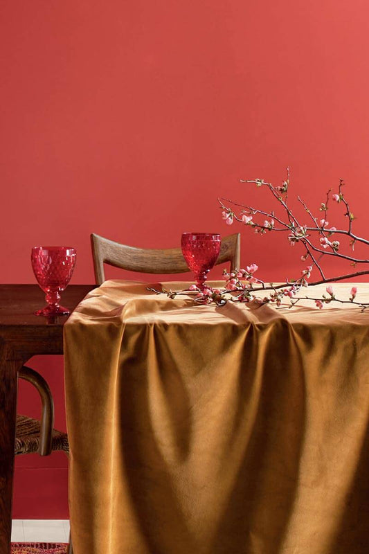 Dining room with coral tinged with pink painted wall, a table, chairs, cups and a branch with buds